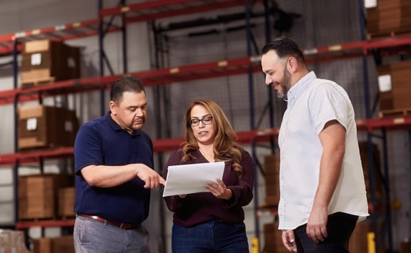 A group of coworkers examining paper plans in a storage room