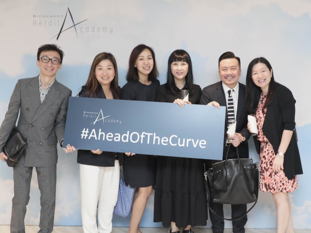 A group of coworkers in China holding a recognition table from Richemont's Retail Academy with a slogan on it Ahead of the Curve