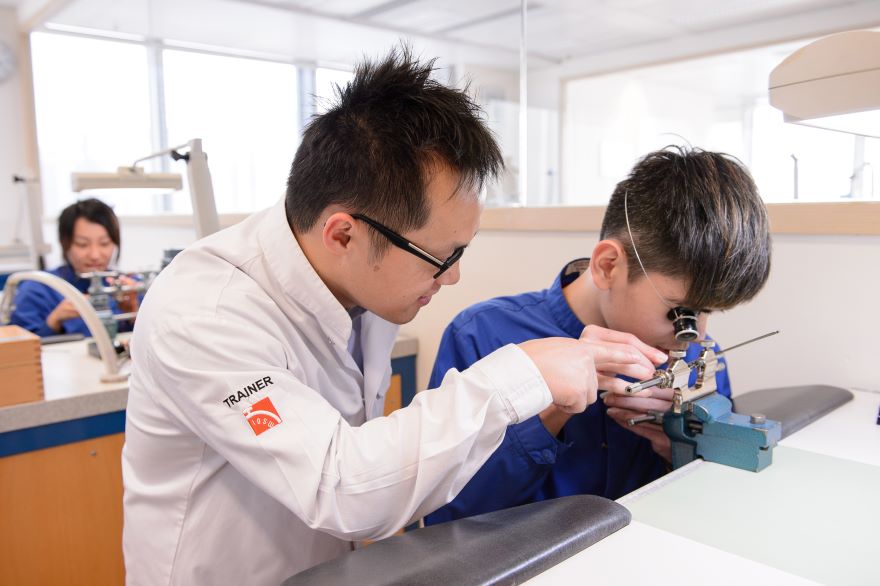 A watchmakers giving instructions to an intern while examining a watch